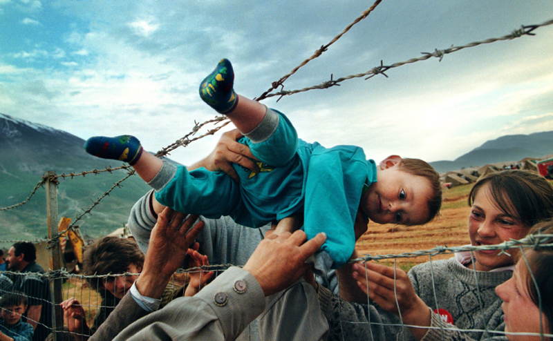 Dvojročný utečenec z Kosova, Agim Shala, je podávaný cez ostnatý plot do rúk prarodičov v tábore utečencov v Kukes v Albánsku.