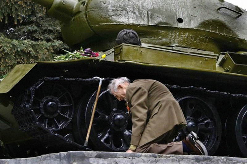 Ruský veterán plače pod sovietskym tankom, ktorý sa používal počas druhej svetovej vojny.