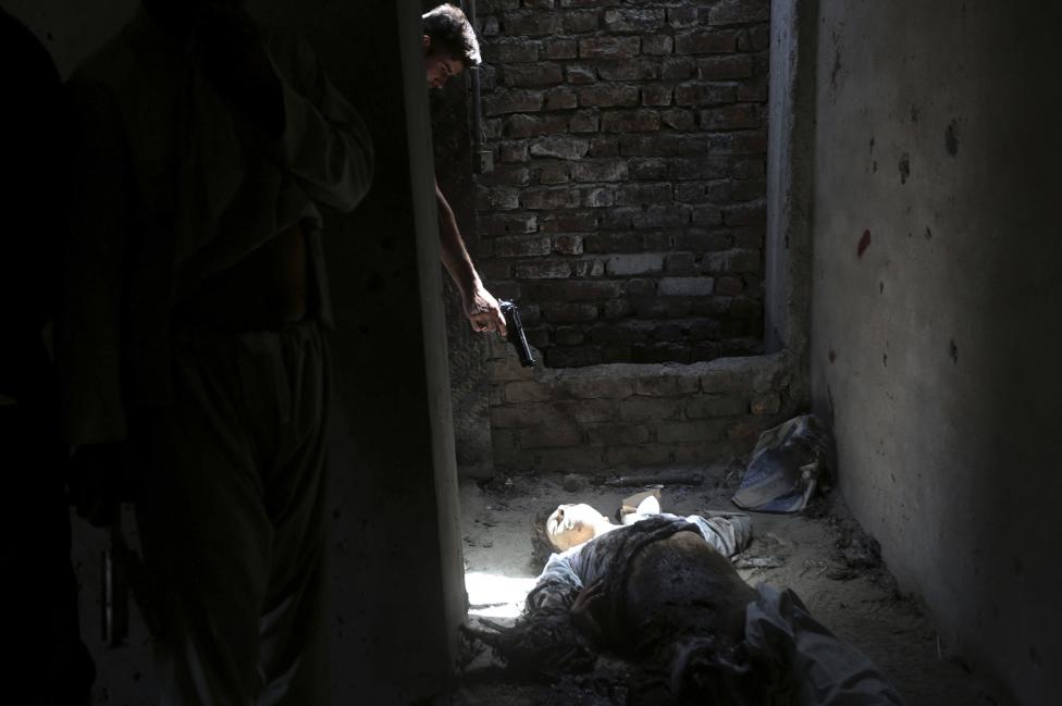 Afgánsky vojak mieri zbraňou na mŕtve neznáme telo a ukazuje tak nenávisť k povstalcom po útoku na letisko v Kábule. 17.7.2014.