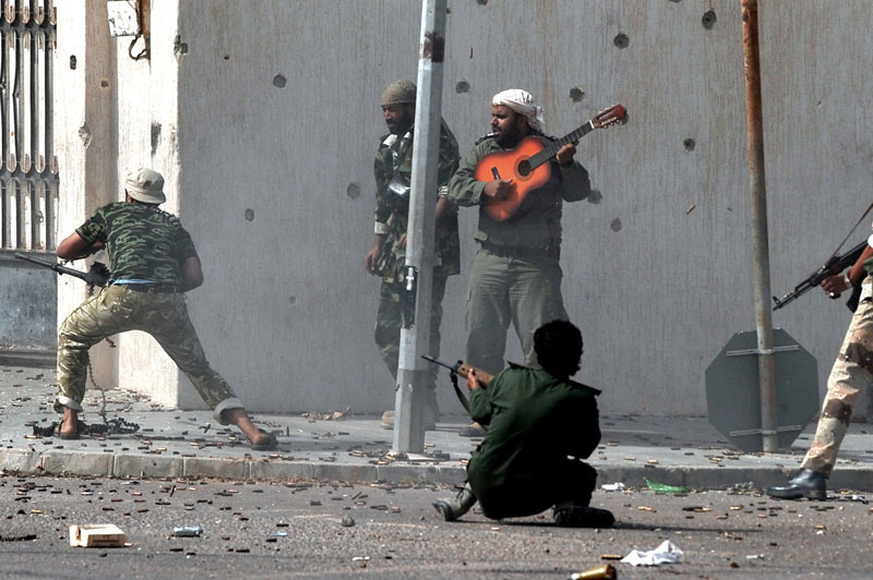 Na prvej fotografii Arisa Messinisa vidíme scénu z lýbijskej občianskej vojny z roku 2011. Práve prebiehala prestrelka medzi stúpencami Kaddáfího a rebelmi, ale ani to nezabránilo neznámemu mužovi, aby len tak na ulici hral na svojej gitare. Ako sám Aris povedal, neznámy gitarista sa snažil povzbudiť ostatných bojovníkov, ale priamo boja sa sám nezúčastnil, zostal verný svojej hudbe.