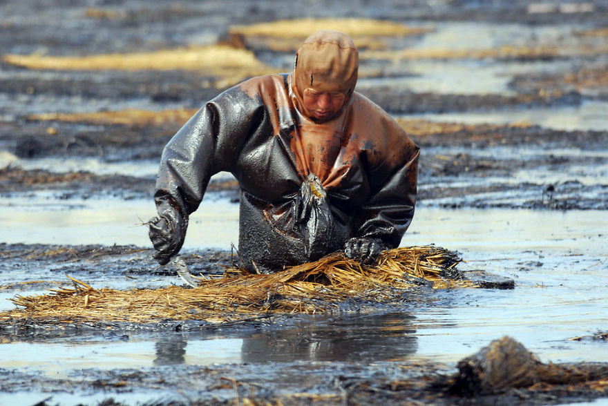 Robotník sa snaží vyčisiť vodu od oleja, Dalian.