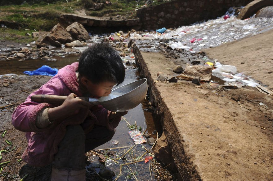 Dieťa pije vodu v blízkosti potoka v provincii Yunnan.
