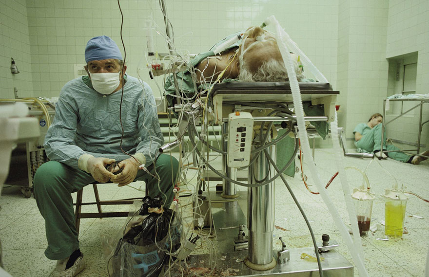 Srdcový chirurg sedí úplne vyčerpaný po 23-hodinovej transplantácii srdca. Jeho asistent spí v rohu.